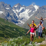 Une famille de 4 personnes avec enfants sur les épaules qui randonne en été à serre chevalier.