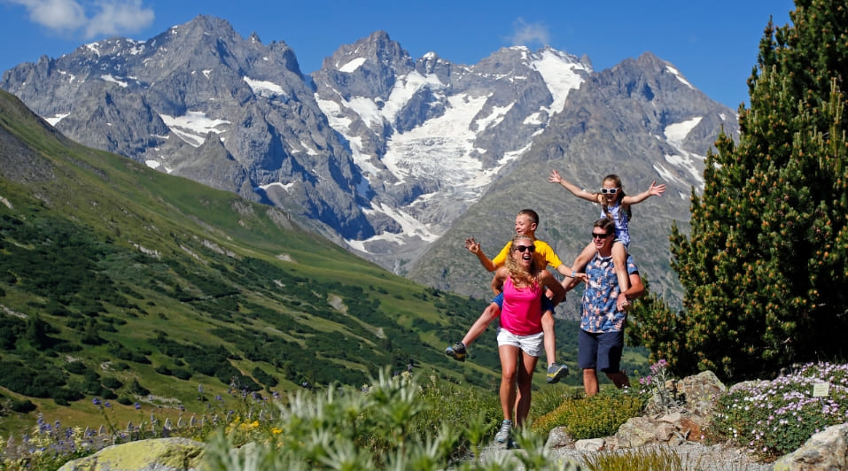 Une famille de 4 personnes avec enfants sur les épaules qui randonne en été à serre chevalier.