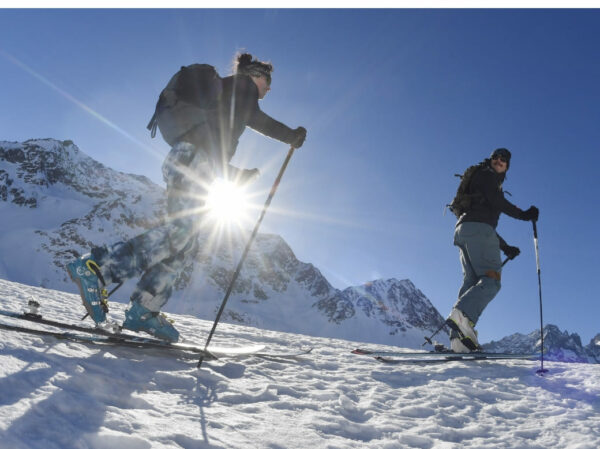 Couple en ski de randonnée par une belle journée ensoleillée, sommets enneigés.